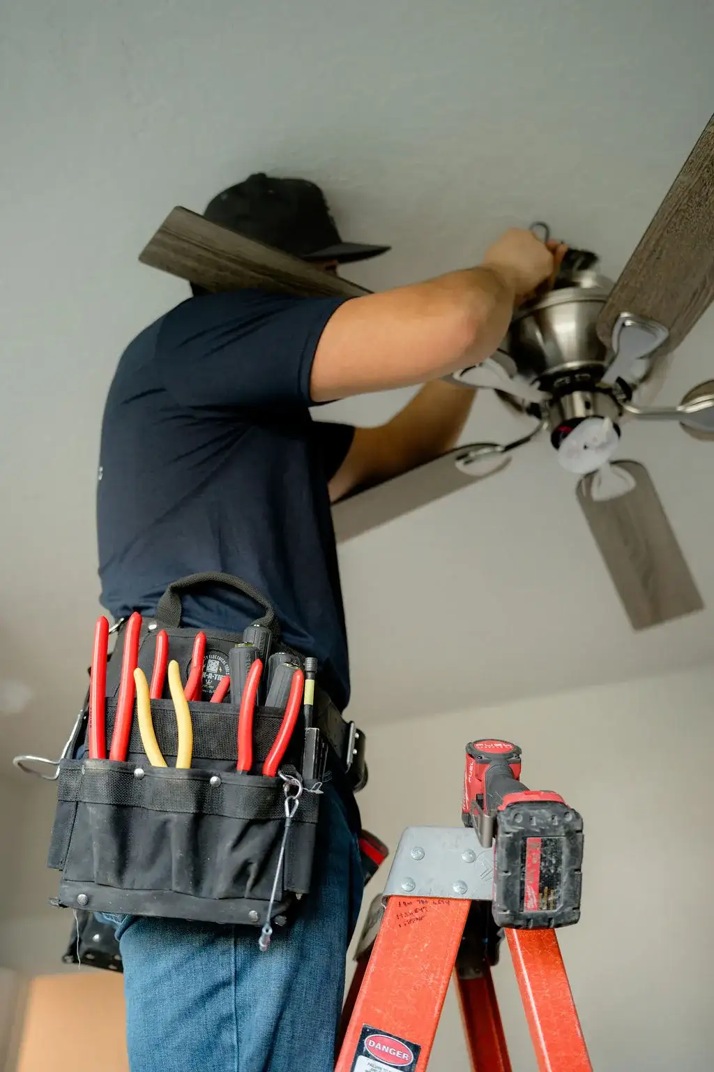 Electrician with a tool belt full of pliers and screwdrivers installing a ceiling fan