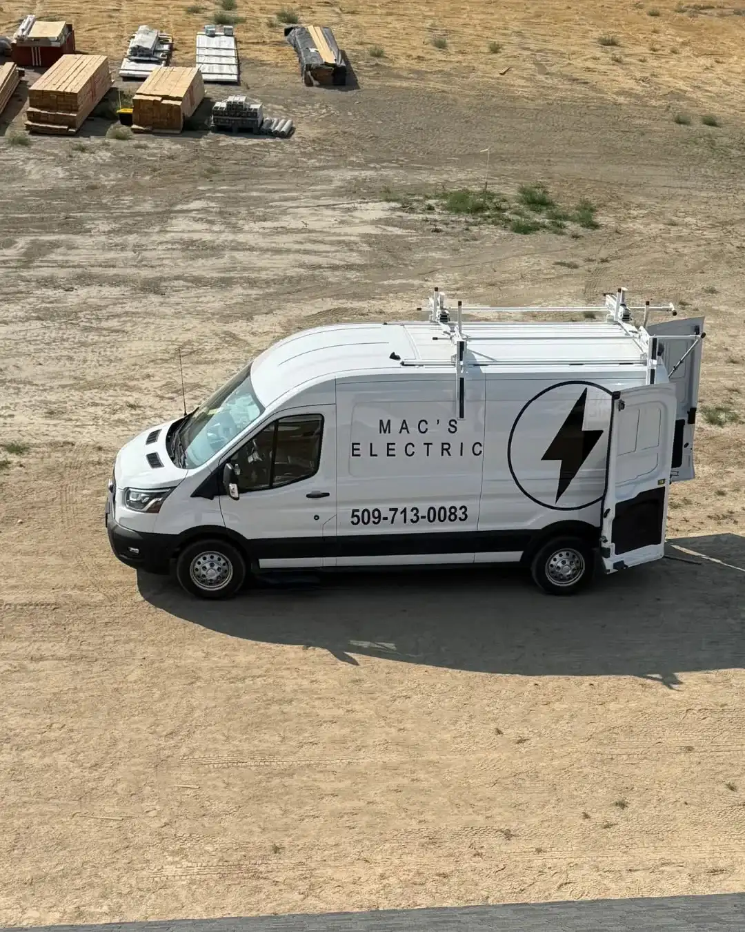 The MAC's Electric work van parked on a dirt job site, with stacks of lumber behind it